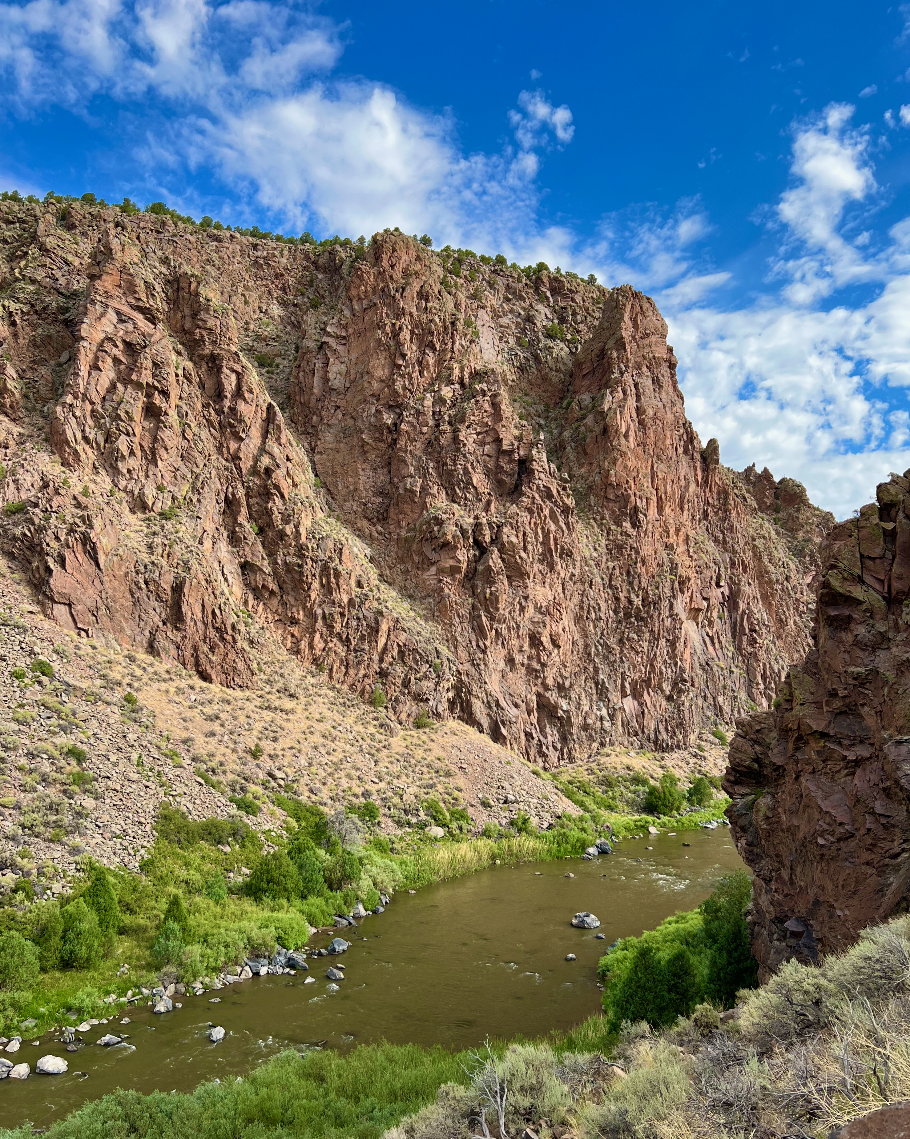North-central New Mexico landscape includes red-rock cliffs, a river and greenery.