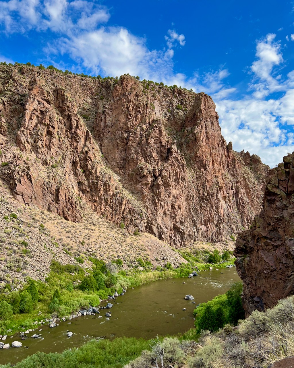 North-central New Mexico landscape includes red-rock cliffs, a river and greenery.